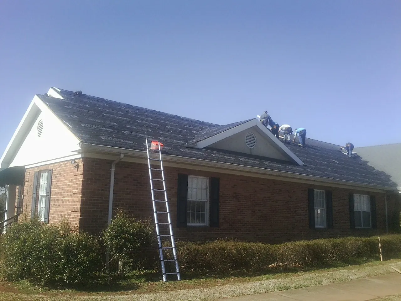 Crew tearing shingles off a brick ranch roof with a ladder set — Metal Roof Repair work by our crew in Aledo