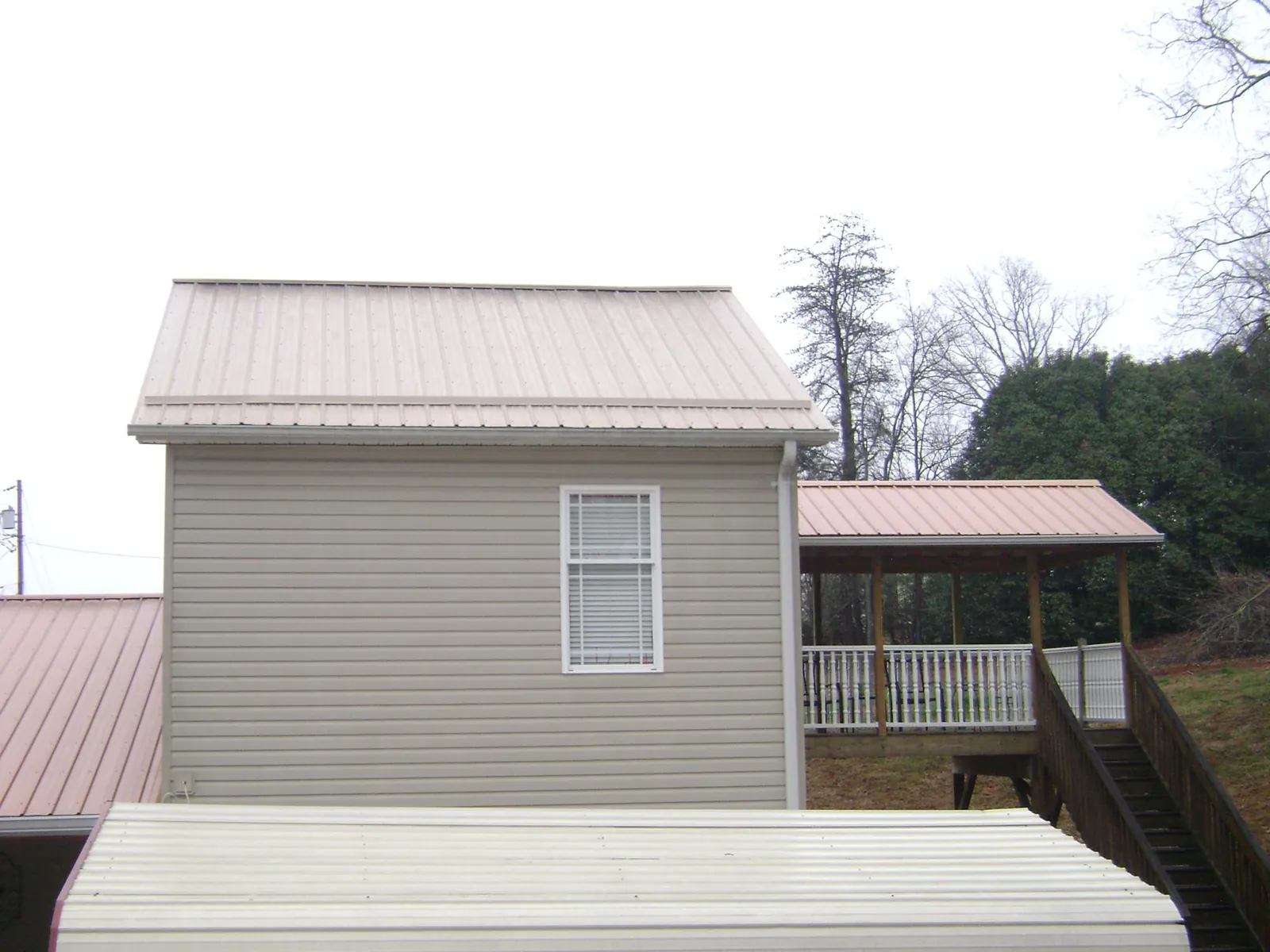 Tan metal roofs on a two story addition and attached porch, from a Roof Replacement job in Aledo